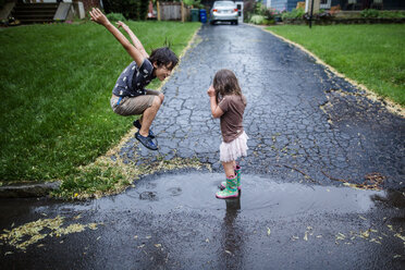 Side view of playful siblings enjoying on wet road during rainy season - CAVF50657