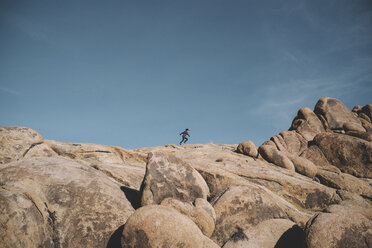 Mid distance view of boy running on rock formations against sky at desert - CAVF50691