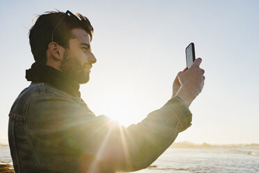 Seitenansicht eines Mannes beim Fotografieren am Strand gegen den klaren Himmel bei Sonnenuntergang - CAVF50736