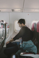 Side view of man using mobile phone while traveling in airplane - CAVF50737