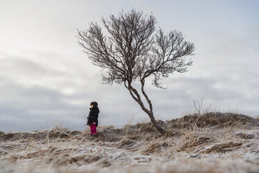 Mädchen stehend an einem kahlen Baum gegen den Himmel auf einem Feld - CAVF50747