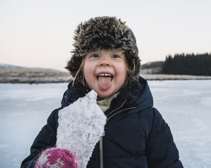 Portrait of playful girl sticking out tongue while holding ice during winter - CAVF50748