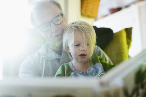 Niedriger Blickwinkel von Großvater mit Enkelin beim Lesen eines Buches, während sie zu Hause sitzen - CAVF50751
