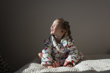 Smiling girl with eyes closed sunbathing while sitting on bed at home - CAVF50760