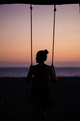 Rear view of silhouette woman swinging at beach against sky during sunset - CAVF50772