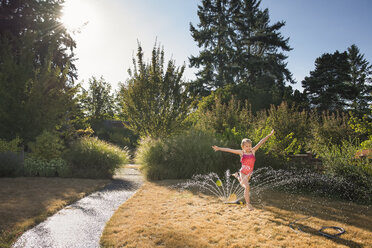 Girl jumping over sprinkler at yard - CAVF50799