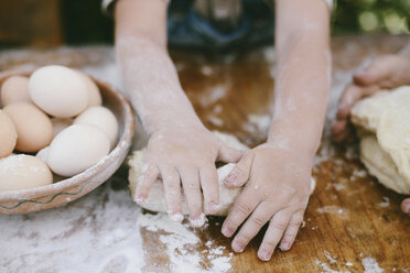 Cropped hands of mother and son kneading dough on wooden table at yard - CAVF50818