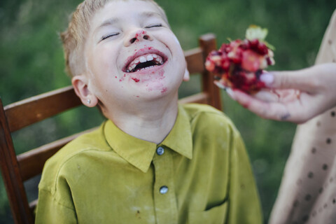 Cropped hand of mother feeding sweet pie to happy son sitting on chair at yard stock photo