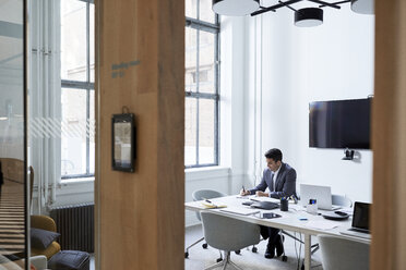 Businessman working at conference table in board room seen from doorway - CAVF50839