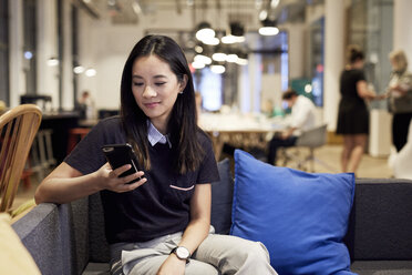 Confident businesswoman using mobile phone while sitting on sofa at creative office - CAVF50844