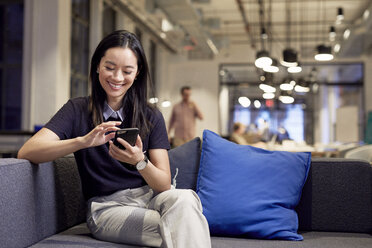 Smiling businesswoman using mobile phone while sitting on sofa at office - CAVF50845