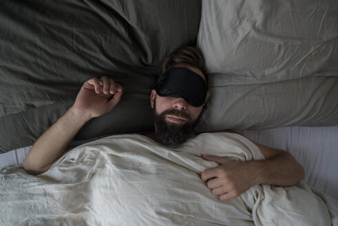High angle view of man wearing sleep mask while sleeping on bed at home - CAVF50859