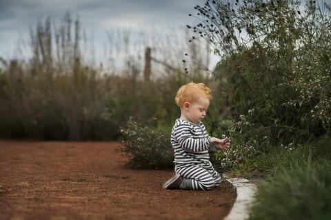 Seitenansicht eines kleinen Jungen, der einen Stock hält, während er im Park kniet, lizenzfreies Stockfoto