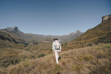 Rear view of woman with backpack hiking on grassy field against clear blue sky - CAVF50882