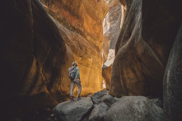 Rear view of female hiker with backpack standing on rocks - CAVF50886