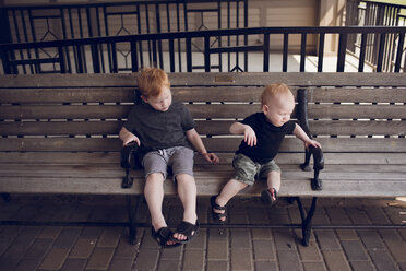 Brüder sitzen auf einer Holzbank im Park - CAVF50894