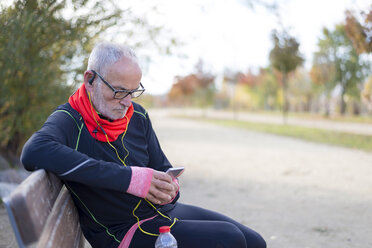 Senior man using smart phone while listening music on park bench - CAVF50898