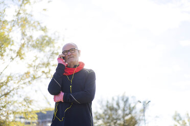 Älterer Mann in Sportkleidung beim Telefonieren mit dem Smartphone gegen den Himmel im Park - CAVF50899