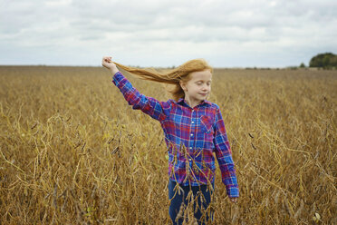 Carefree girl with eyes closed holding her hair while standing amidst soybean's field against sky - CAVF50902