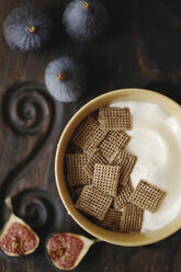 Draufsicht auf Vanillejoghurt mit Crackern in einer Schüssel neben Feigen auf einem Schneidebrett - CAVF50915