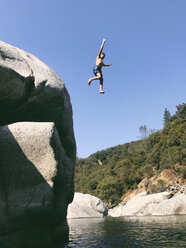 Niedriger Blickwinkel auf einen unbekümmerten, hemdlosen Jungen, der von einer Klippe in den Yuba River springt - CAVF50924