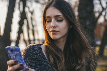 Nahaufnahme einer Frau, die im Park ein Mobiltelefon benutzt - CAVF50930