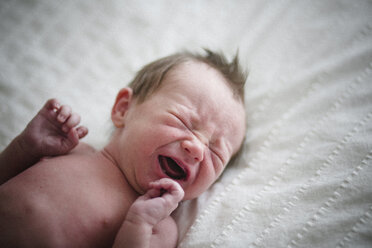 High angle view of shirtless newborn baby boy crying on bed at home - CAVF50977