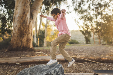 Side view of boy jumping on rock in forest - CAVF50987