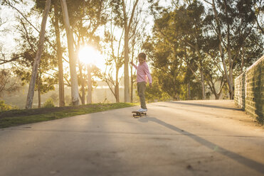 Seitenansicht eines Jungen, der bei Sonnenuntergang auf dem Fußweg im Park Skateboard fährt - CAVF50990