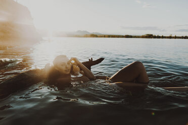 Porträt einer selbstbewussten jungen Frau, die in einem See schwimmt, gegen den Himmel an einem sonnigen Tag - CAVF50993