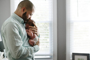 Seitenansicht eines Vaters, der seine neugeborene Tochter küsst, während er sie zu Hause trägt - CAVF50997