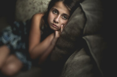 Hochformatiges Porträt eines traurigen Mädchens auf dem Sofa sitzend - CAVF51003