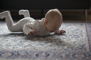 Weinendes kleines Mädchen auf dem Teppich liegend und mit den Beinen strampelnd - JLOF00269