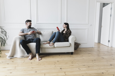 Ein Paar sitzt zu Hause auf der Couch und benutzt seine Smartphones, lizenzfreies Stockfoto