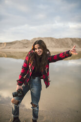 Porträt einer lachenden jungen Frau mit Kamera am Strand - RAEF02191
