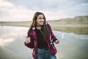 Porträt einer lächelnden jungen Frau, die ein Selfie mit ihrem Smartphone am Strand macht - RAEF02195