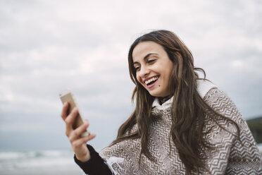 Porträt einer lachenden jungen Frau, die auf ihr Mobiltelefon schaut - RAEF02205