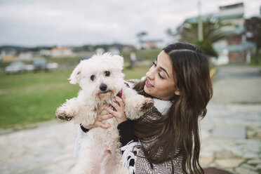 Young woman holding cute white dog - RAEF02206