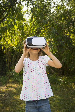 Erstauntes kleines Mädchen mit Virtual-Reality-Brille im Garten, lizenzfreies Stockfoto