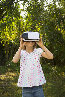 Erstauntes kleines Mädchen mit Virtual-Reality-Brille im Garten - LVF07490