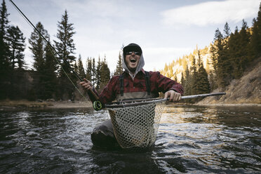 Cheerful man screaming while fishing in river against sky at forest - CAVF51031