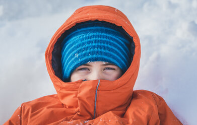 Hochwinkliges Porträt eines Jungen in warmer Kleidung auf einem schneebedeckten Feld liegend - CAVF51055