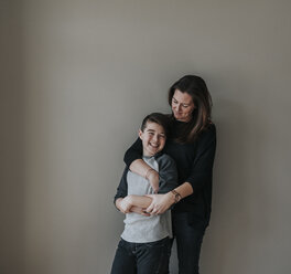 Happy mother with son standing by wall at home - CAVF51058