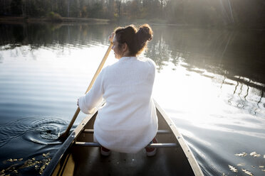 Rückansicht einer Frau, die in einem Boot auf einem See im Wald sitzt - CAVF51074