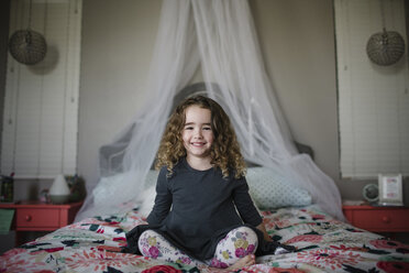 Porträt eines fröhlichen Mädchens, das zu Hause auf dem Bett sitzt - CAVF51081