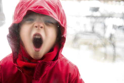Porträt eines verspielten Jungen, der warme Kleidung trägt, während er das Fenster mit Atemdampf beschlägt - CAVF51085