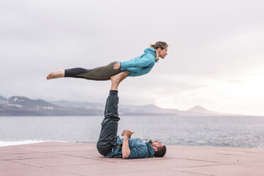 Full length of friends practicing acroyoga on promenade by sea - CAVF51091