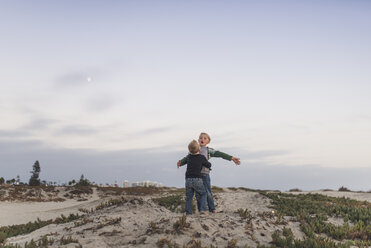 Brüder spielen im Sand am Strand gegen den Himmel - CAVF51094