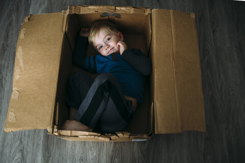 Hochformatiges Porträt eines Jungen, der zu Hause in einem Karton liegt, lizenzfreies Stockfoto