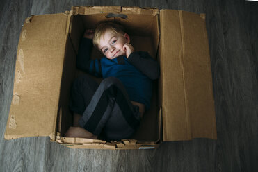 Hochformatiges Porträt eines Jungen, der zu Hause in einem Karton liegt - CAVF51106